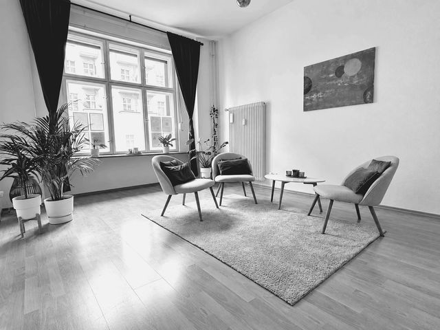 Heller Praxisraum in Berlin-Friedrichshain mit drei Sesseln um einen kleinen Tisch, großem Fenster und Pflanzen
